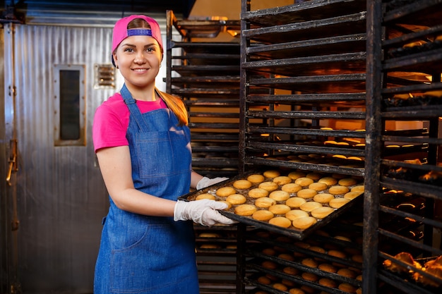 Una panadera profesional sostiene una bandeja con galletas frescas en sus manos. Pasteles dulces en una panadería