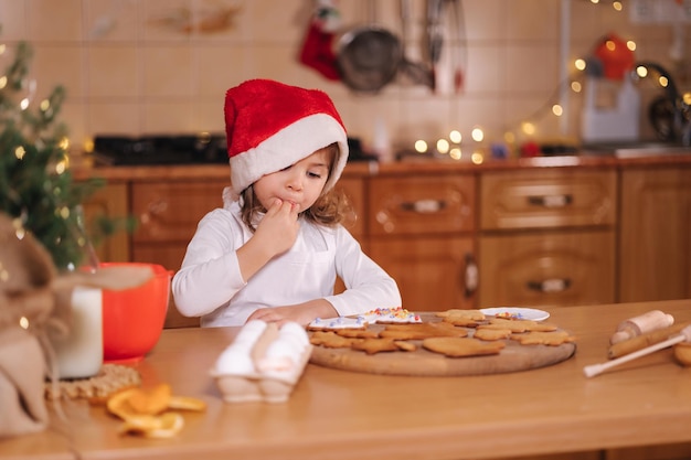 Panadería casera cocinando dulces festivos tradicionales niña en rojo gorro de Papá Noel preparándose para hacer