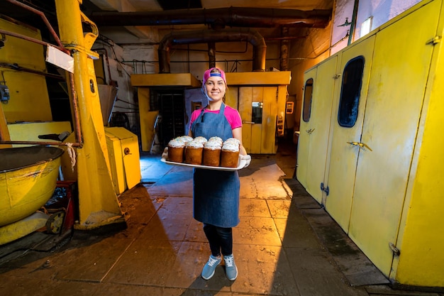 Panadería joven feliz trabajando en una gran fábrica. Panadero femenino en uniforme en la cocina profesional.