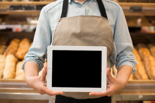 Foto panadería vendedor permanente mostrando tableta frente diferentes pasteles