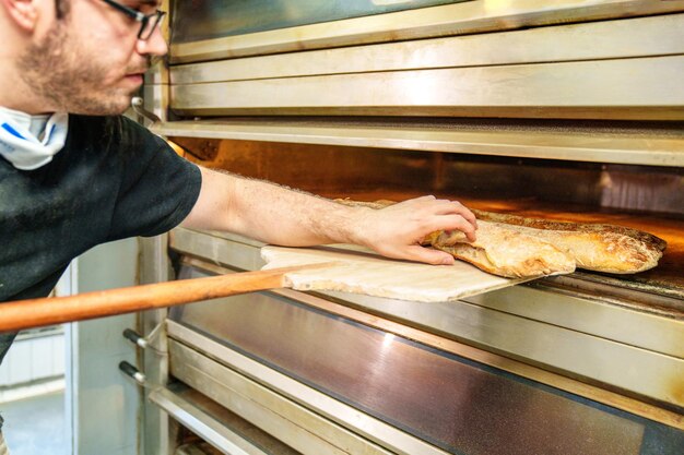 Foto un panadero artesano saca una baguete con corteza dorada de un horno de panadería mostrando habilidad y tradición
