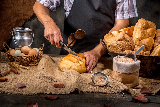 Panadero cortando pan en mesa rústica.