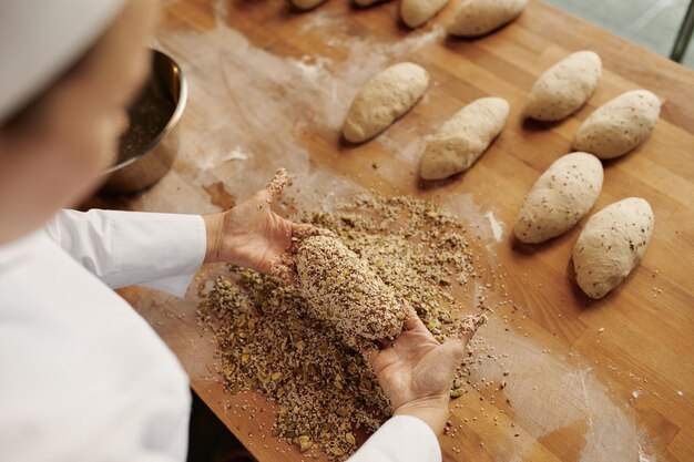 Panadero dando forma a bagels de pan, mojando la masa con semillas y copos de avena. Concepto de casa de panadería