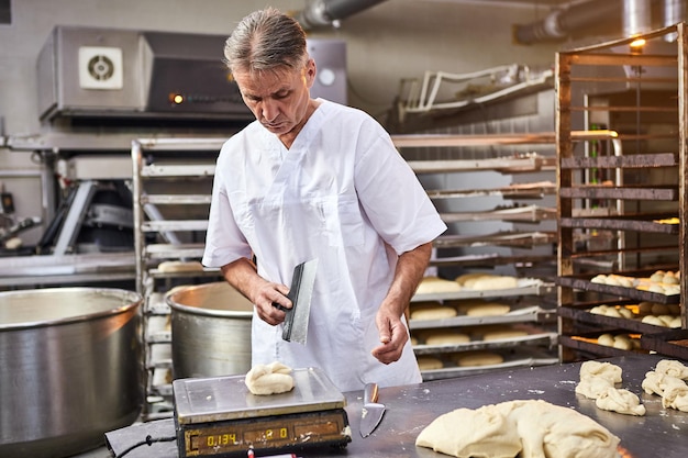 Panadero experto que divide la masa cruda en porciones iguales y las pesa Proceso de hacer pan en panadería