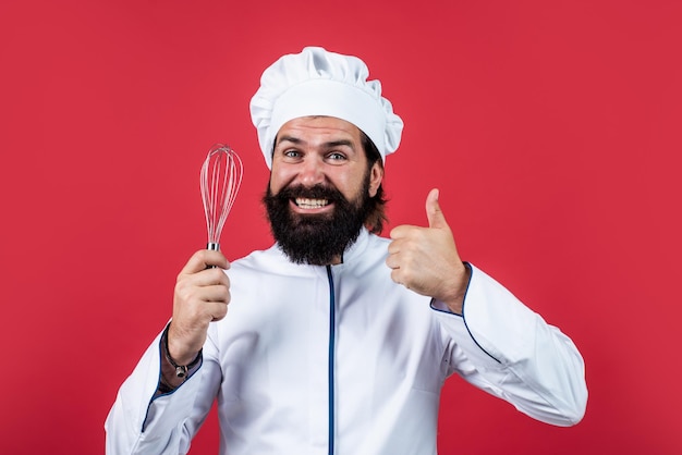 El panadero habilidoso usa utensilios de cocina para cocinar. El chef con sombrero prepara una comida saludable. Un hombre guapo con barba y bigote cocina comida. Restaurante profesional. Cocinero para hornear.