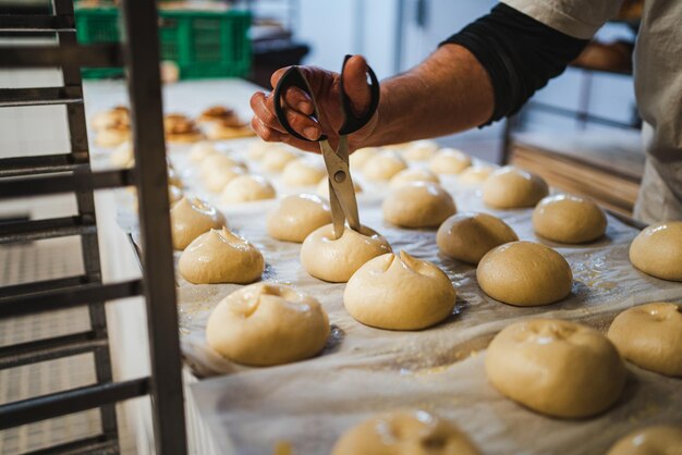 Panadero haciendo cortes con tijeras en bollo de leche cruda antes de hornear