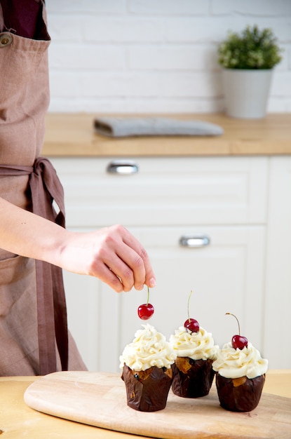 Panadero hembra decorando cupcake con cereza y crema.