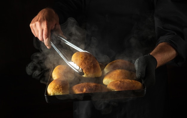 El panadero hornea pasteles o bollos en una bandeja para hornear caliente sacada del horno Espacio negro para menú o receta