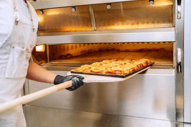 panadero lleva una bandeja de palmas de hojaldre en sus manos y la está poniendo en el horno de la panadería