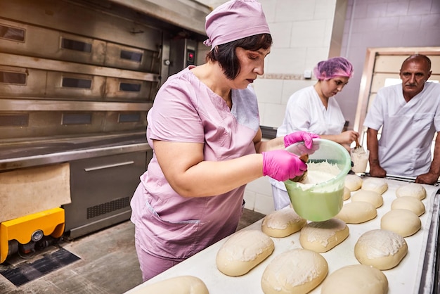 Panadero profesional en uniforme unta masa de pan de mantequilla para hornear en la fabricación de panadería en el fondo de colegas