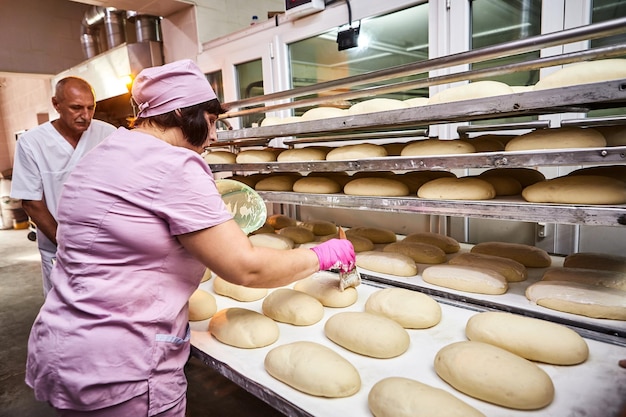 Panadero profesional en uniforme unta masa de pan de mantequilla para hornear en la fabricación de panadería en el fondo de colegas