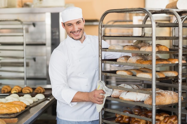 Foto panadero sonriente empujando la bandeja de pan