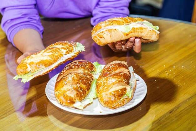 panaderos mano mostrando un sándwich con pan abierto con lechuga de jamón de queso y mayonesa en un plato en una mesa para el desayuno
