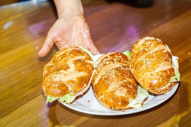 panaderos mano mostrando un sándwich con pan abierto con lechuga de jamón de queso y mayonesa en un plato en una mesa para el desayuno