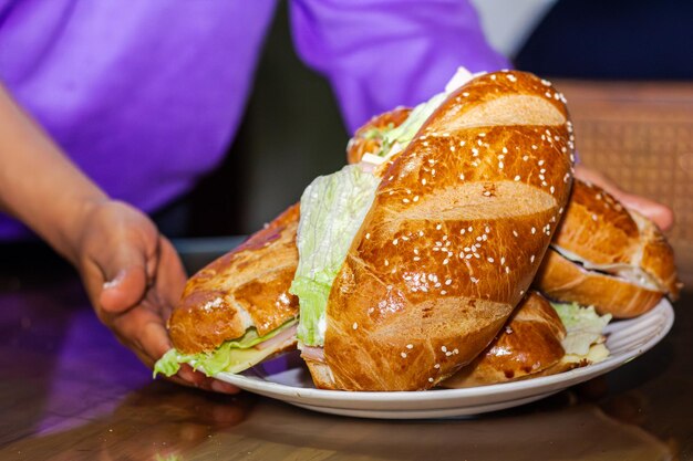 Foto panaderos mano mostrando un sándwich con pan abierto con lechuga de jamón de queso y mayonesa en un plato en una mesa para el desayuno