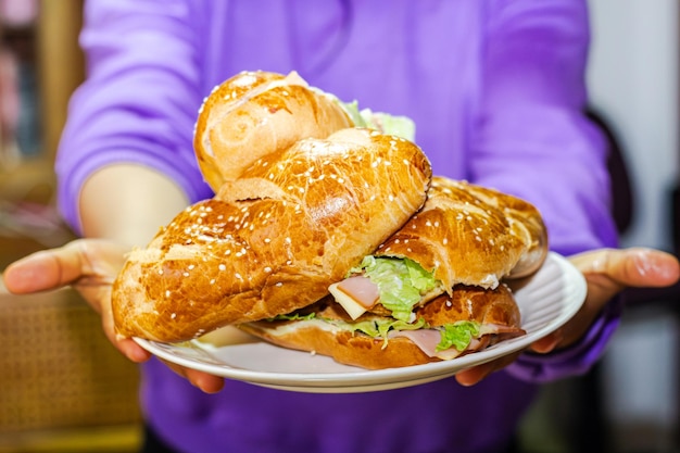 Foto panaderos mano mostrando un sándwich con pan abierto con lechuga de jamón de queso y mayonesa en un plato en una mesa para el desayuno