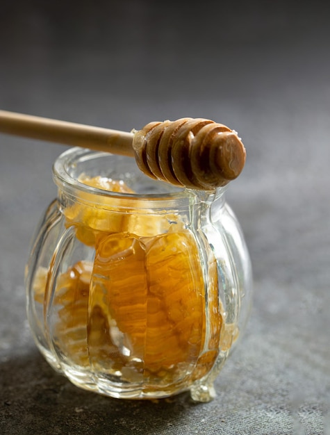 Panal de miel sellado con cucharón de madera para mezclar y degustar miel natural en un pequeñ...