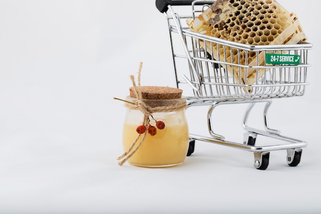 Panal en un mini carrito de compras. Un vaso de miel natural cerca del carrito de la compra.