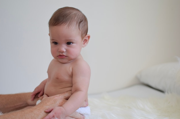 Pañal de tela con pañal para bebé intente sentarse apoyado por las manos del padre en la cama blanca