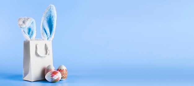 Pancarta ancha sobre un fondo azul El concepto de compras en línea para compras y ventas de Pascua para las vacaciones Bolsa de regalo con orejas de conejo y huevos de Pascua Foto de alta calidad