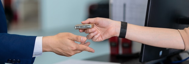 Pancarta y portada de la mano de la recepcionista asiática de primer plano que recibe la llave automática del automóvil para verificar en el centro de servicio de mantenimiento en la sala de exposición