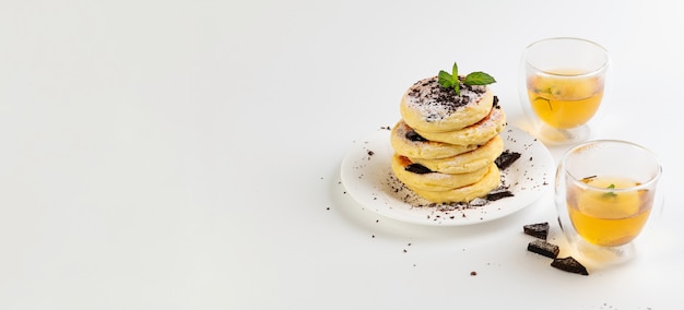 Foto pancarta, tortas de queso sin gluten sobre harina de coco con chocolate y té verde, sobre un fondo blanco.