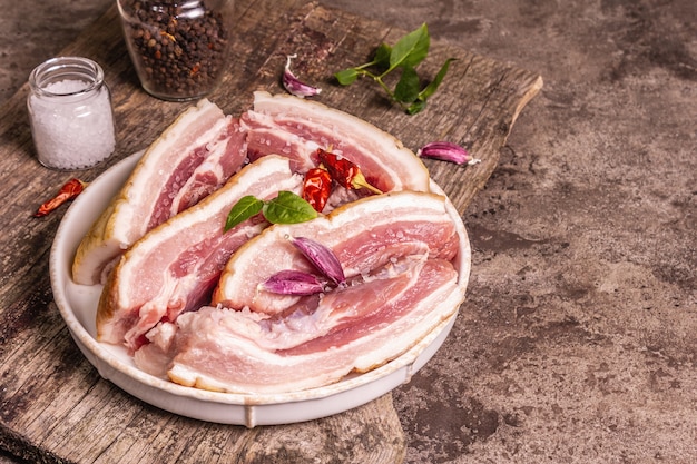 Panceta de cerdo cruda con corteza, carne de peritoneo. Especias y hierbas, ingredientes para cocinar comidas saludables, proteínas animales. Fondo de hormigón de piedra, espacio de copia