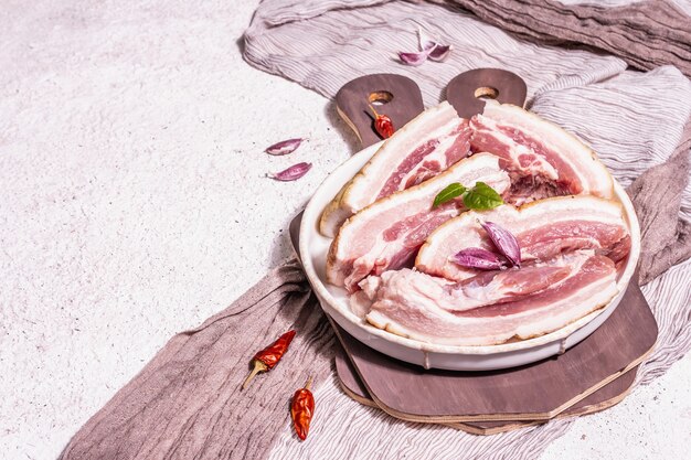 Foto panceta de cerdo cruda con corteza, carne de peritoneo. especias y hierbas, ingredientes para cocinar comidas saludables, proteínas animales. fondo de yeso claro, espacio de copia