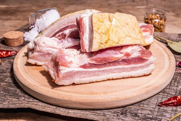 Panceta de cerdo cruda con corteza, carne de peritoneo. Especias y hierbas, ingredientes para cocinar comidas saludables, proteínas animales. Mesa de madera vintage, espacio de copia