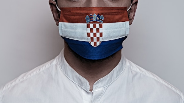 Pandemia de coronavirus. Concepto de cuarentena del virus Corona, Covid-19. El rostro masculino está cubierto con una máscara médica protectora, pintada con los colores de la bandera de Croacia.