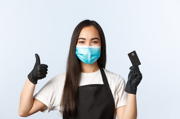 Pandemia Covid-19, cafetería, pequeña empresa y concepto de prevención de virus. Sonriente y linda barista asiática, consejos de camarera, use el método de pago sin contacto, mantenga la tarjeta de crédito