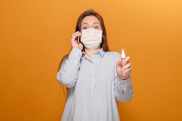 Pandemia de coronavírus, retrato de close-up de jovem em fundo amarelo, falando no telefone, pânico, spray anti-séptico na mão