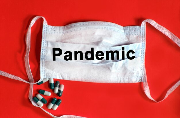 PANDEMIA - texto en una mascarilla protectora, tabletas sobre un fondo rojo.