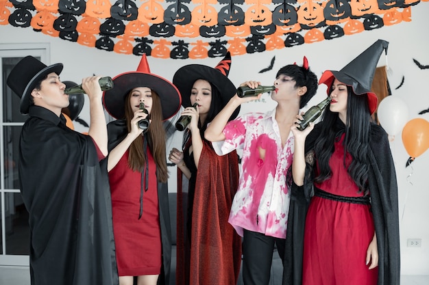 Pandilla de jóvenes asiáticos en traje de bruja, mago con celebrar la fiesta de Halloween para bailar y beber y borracho en la habitación. Grupo adolescente tailandés con celebrar Halloween. Concepto fiesta Halloween en casa.