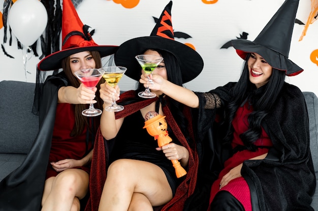 Pandilla de mujeres tailandesas adolescentes brujas con celebrar la fiesta de Halloween con una sonrisa en la habitación de su casa. Concepto de fiesta de Halloween en casa. Grupo de mujeres asiáticas jóvenes en traje de bruja celebran en el día de Halloween.