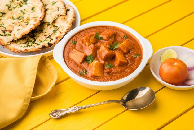 Paneer Butter Masala o Cheese Cottage Curry, popular menú indio de almuerzo y cena servido en Karahi con Naan o Roti sobre fondo cambiante, enfoque selectivo