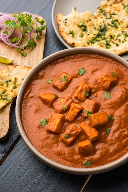 Paneer Butter Masala o Cheese Cottage Curry, popular menú indio de almuerzo y cena servido en Karahi con Naan o Roti sobre fondo cambiante, enfoque selectivo