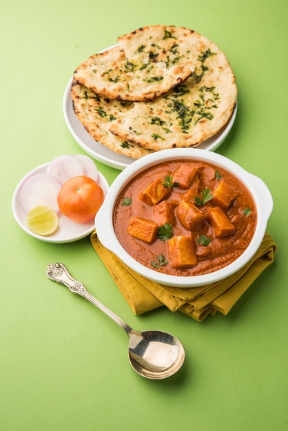 Paneer Butter Masala oder Cheese Cottage Curry, beliebtes indisches Mittag- und Abendessen, serviert in Karahi mit Naan oder Roti über stimmungsvollem Hintergrund, selektiver Fokus