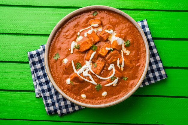Paneer Butter Masala oder Cheese Cottage Curry, beliebtes indisches Mittag- und Abendessen, serviert in Karahi mit Naan oder Roti über stimmungsvollem Hintergrund, selektiver Fokus