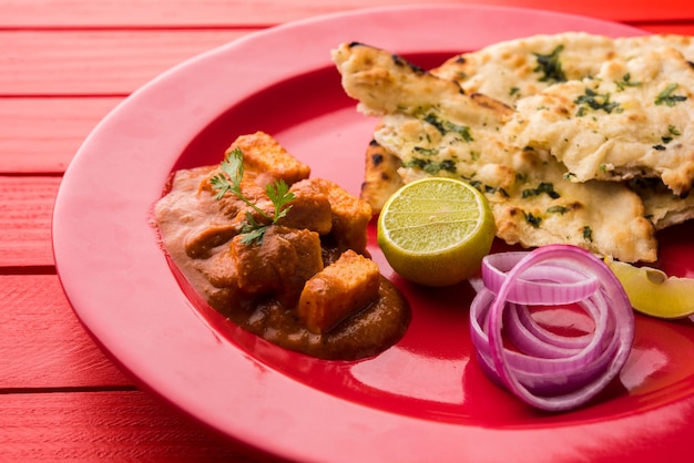 Paneer Butter Masala oder Cheese Cottage Curry, beliebtes indisches Mittag- und Abendessen, serviert in Karahi mit Naan oder Roti über stimmungsvollem Hintergrund, selektiver Fokus