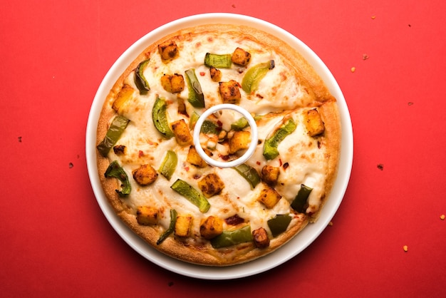 Paneer Pizza é uma versão indiana do prato italiano coberto com queijo cottage, servido em um prato com molho branco. foco seletivo