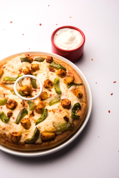 Paneer Pizza ist eine indische Version eines italienischen Gerichts mit Hüttenkäse, serviert auf einem Teller mit weißer Soße. selektiver Fokus