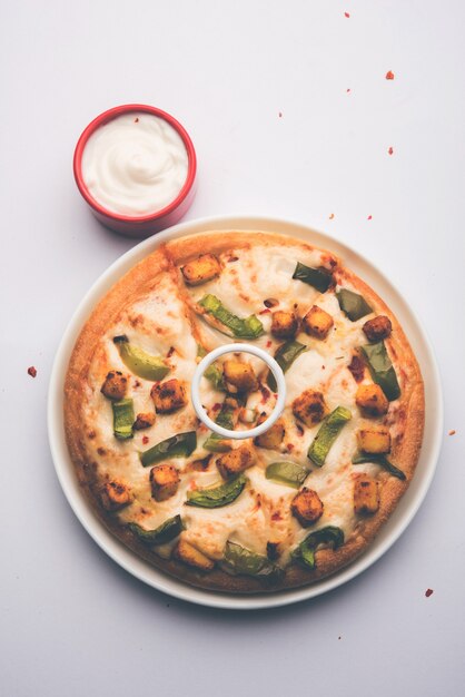 Paneer Pizza ist eine indische Version eines italienischen Gerichts mit Hüttenkäse, serviert auf einem Teller mit weißer Soße. selektiver Fokus