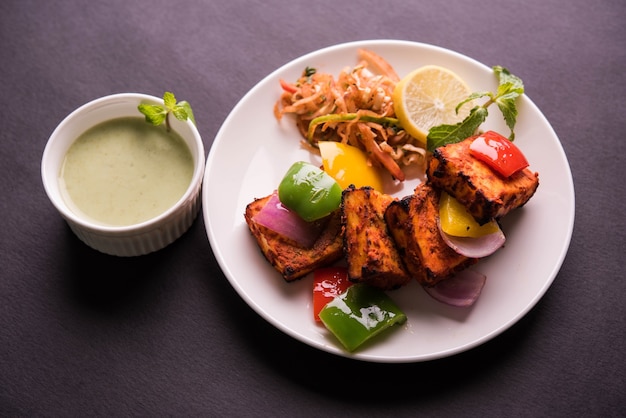 Paneer Tikka ou chilli paneer Kabab - Espetos de queijo indiano Tandoori, servidos em prato branco com pimentão colorido e cebola, com molho verde