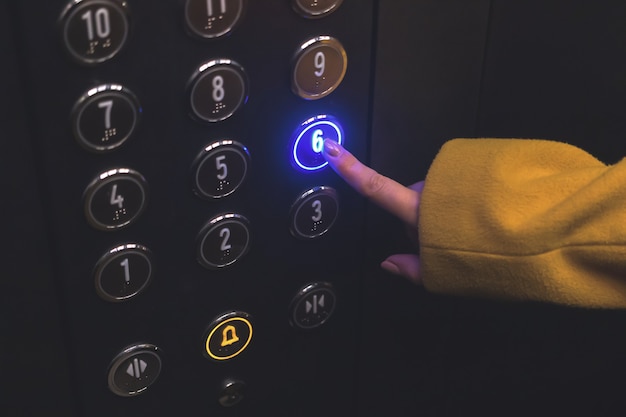 Foto panel del piso del ascensor en el edificio de cerca la mano de la mujer toque y presione el botón en el panel con led ...