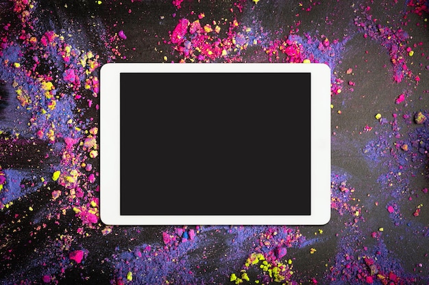 Panel táctil con pantalla en blanco sobre sombras de ojos desmenuzadas de colores o colores holi sobre fondo negro