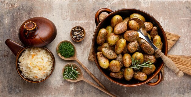 Panela cheia de batatas assadas, filmadas em mesa de madeira rústica os ingredientes incluem batatas cruas alecrim endro sal pimenta e alho
