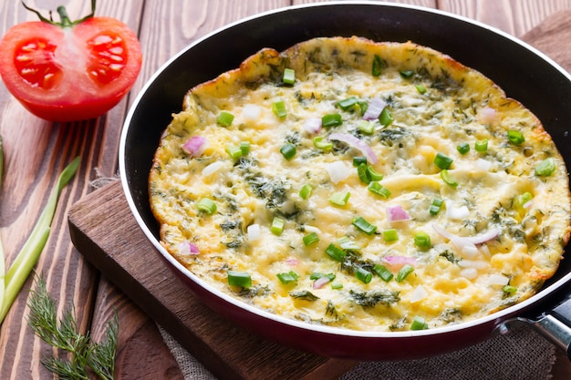 Panela com uma deliciosa omelete em uma tábua sobre um fundo de madeira