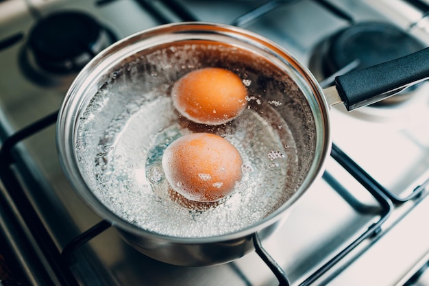 Panela de aço inoxidável com ovos fervendo pequeno-almoço em água em um fogão a gás