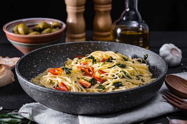 Panela de macarrão italiano cozido. Refeição tradicional de espaguete com legumes e azeitonas na superfície rústica preta